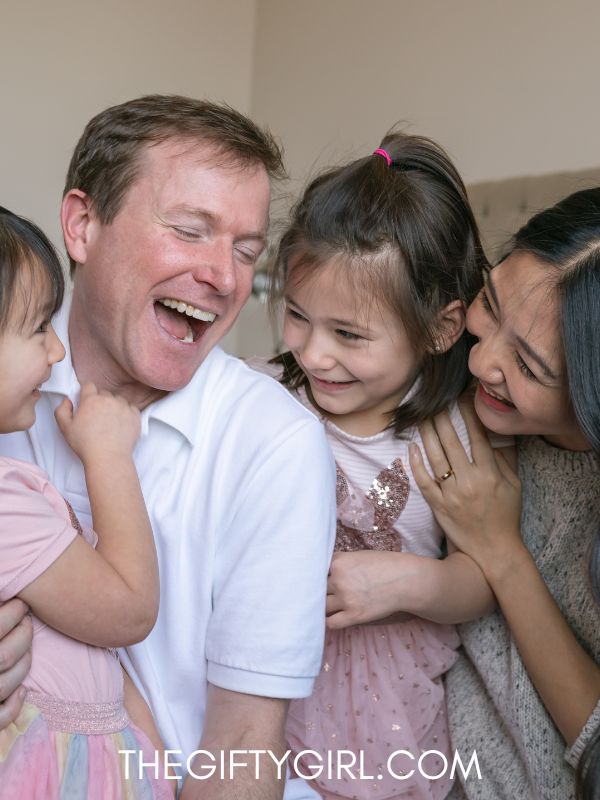 a photo of a family laughing, a mom and dad and two young daughters. 