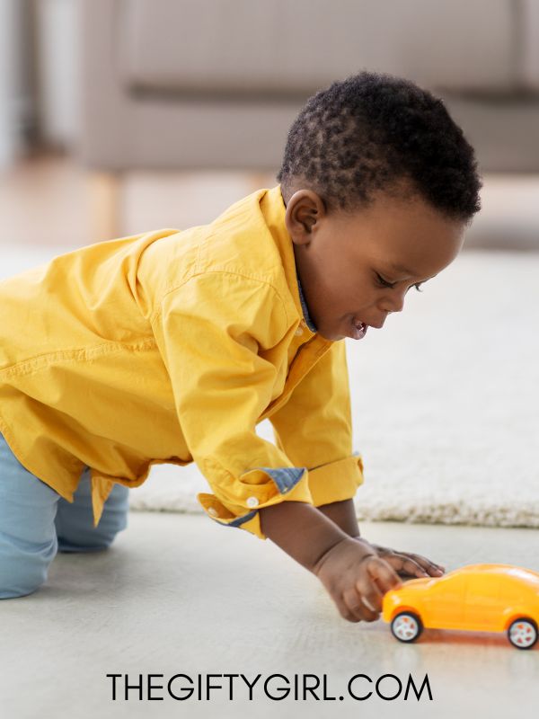 A black boy in a yellow dress shirt plays with a yellow car on the floor. 