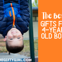 A 4-year-old boy hangs upside down from monkey bars. He is wearing a blue coat with an orange zipper and smiling at the camera. Text overlay says the best gifts for 4-year-old boys The Gifty Gift dot com.