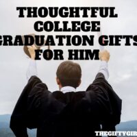 A man stands facing away from the camera. He is wearing a college graduation gown and holding a diploma in one hand and his hat in the other and holding his arms in the air.