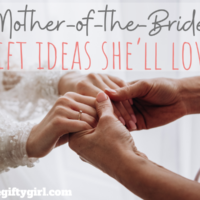 A photograph of a mother holding her daughter's hand the daughter is in a wedding dress. Text overlay says mother of the bride gift ideas she'll love